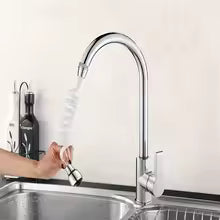 A chrome gooseneck kitchen faucet with a spiral spring pull-down sprayer, shown with a hand turning it on over a stainless steel sink.